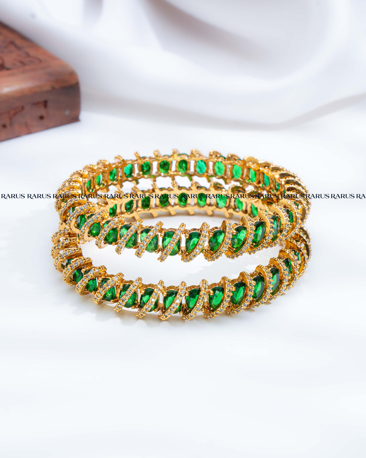 Three stacked gold bangles adorned with marquise-cut green gemstones and small clear accent stones, 