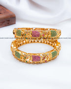 A pair of gold-plated Indian-style elephant bangles decorated with green and pink pavé stones.