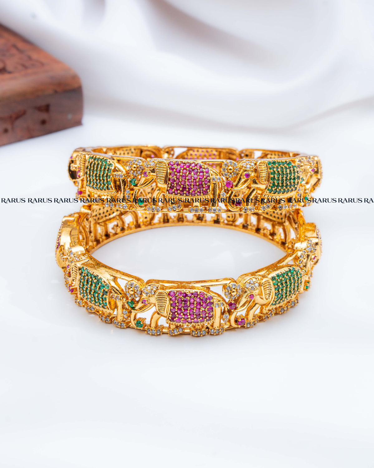 A pair of gold-plated Indian-style elephant bangles decorated with green and pink pavé stones.