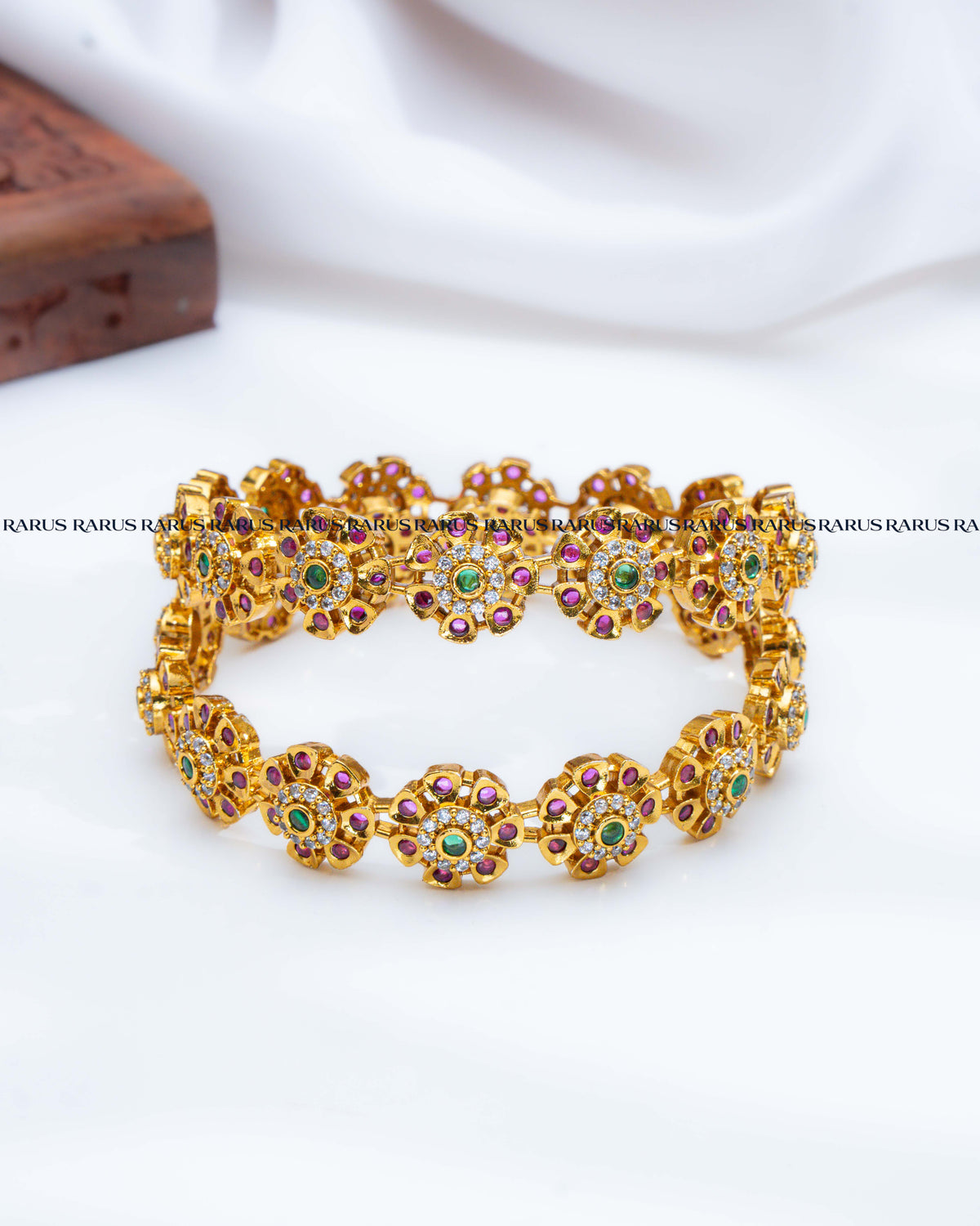 A gold-plated stretch bracelet featuring floral motifs set with small green and pinkish-red stones.