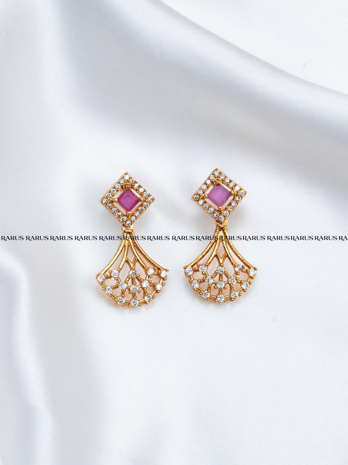 A pair of gold-toned statement earrings with pink rectangular center stones and cascading fan-shaped clusters of small clear stones.