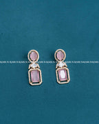 A pair of gold drop earrings with oval pink gemstones and rectangular pink gemstones, accented with small clear stones, displayed on a textured teal background.